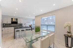 A modern kitchen with white cabinets, a black countertop, and a glass dining table with bar stools.