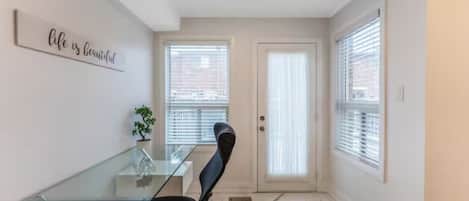 A room with a glass table, a black chair, a potted plant, a door with a window, and a wall sign.