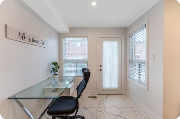 A room with a glass table, a black chair, a potted plant, a door with a window, and a wall sign.