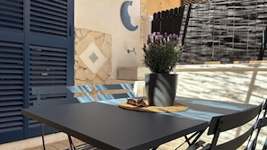 An outdoor seating area with a table, chairs, a potted plant, and a wall-mounted crescent moon decoration. - Zora San Lorenzo - Marzamemi Beach (Reitani)
