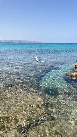 A clear coastal area with a rocky shoreline and a chair floating in the water. - Zora San Lorenzo - Marzamemi Beach (Reitani)
