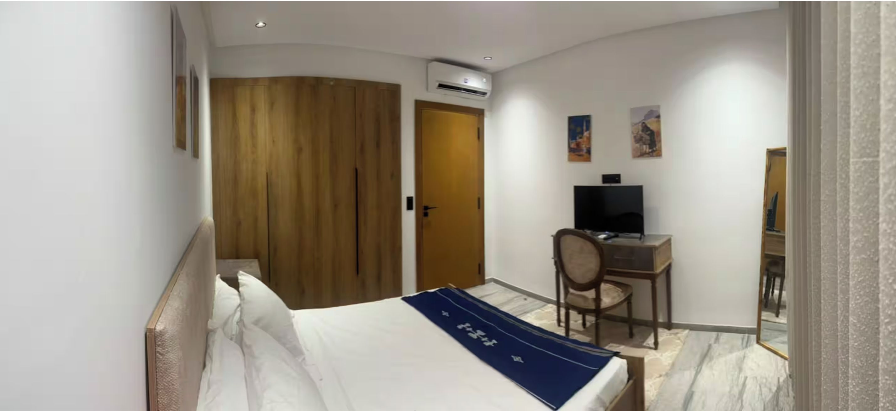 Ein Hotelzimmer mit einem Bett, einem Schreibtisch, einem Stuhl, einer Klimaanlage und Bildern an der Wand.