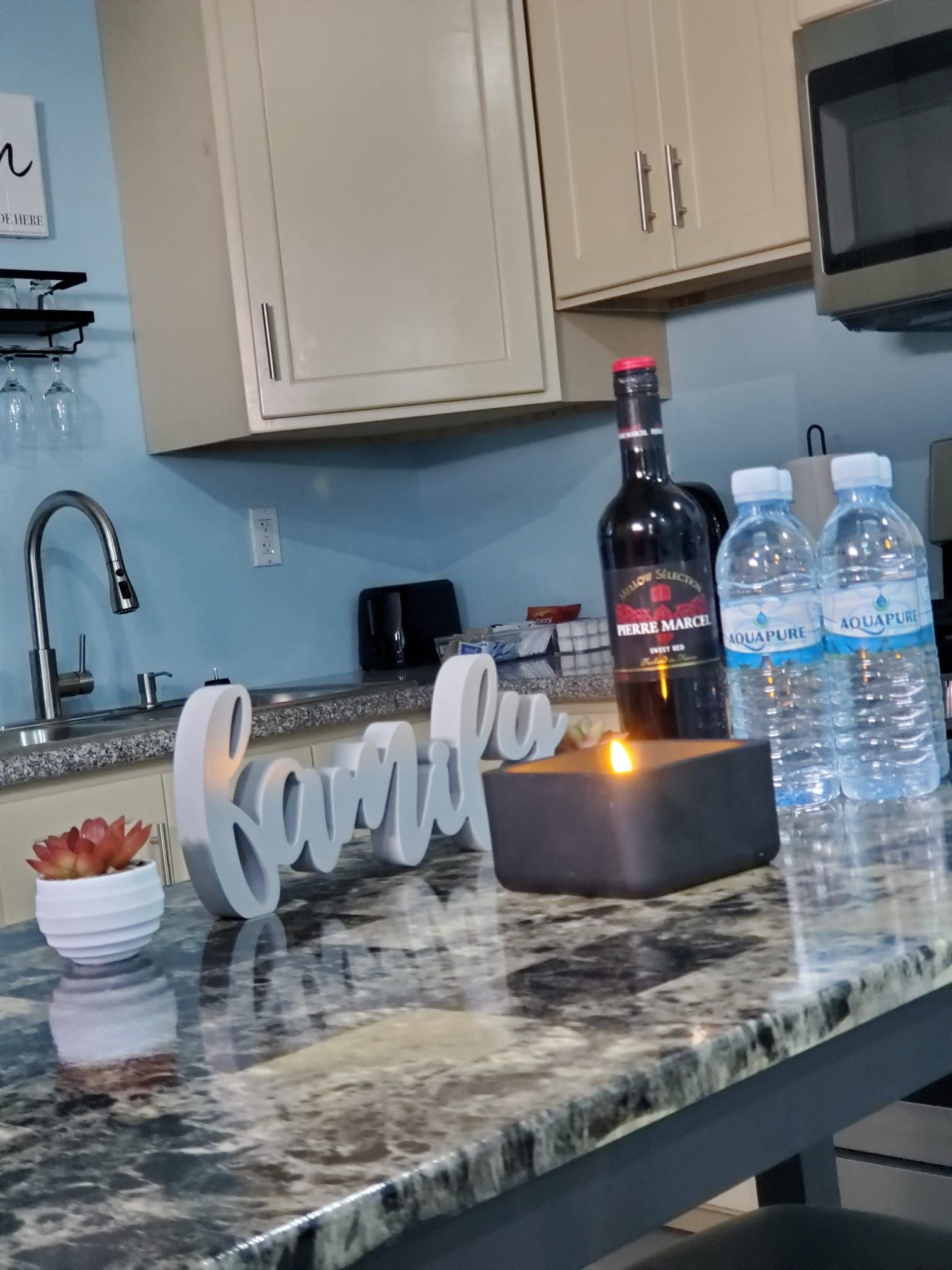 Eine Küchenarbeitsplatte mit einer Flasche Pierre Marcel, zwei Aquapure Wasserflaschen, einer Kerze und einer Sukkulente.