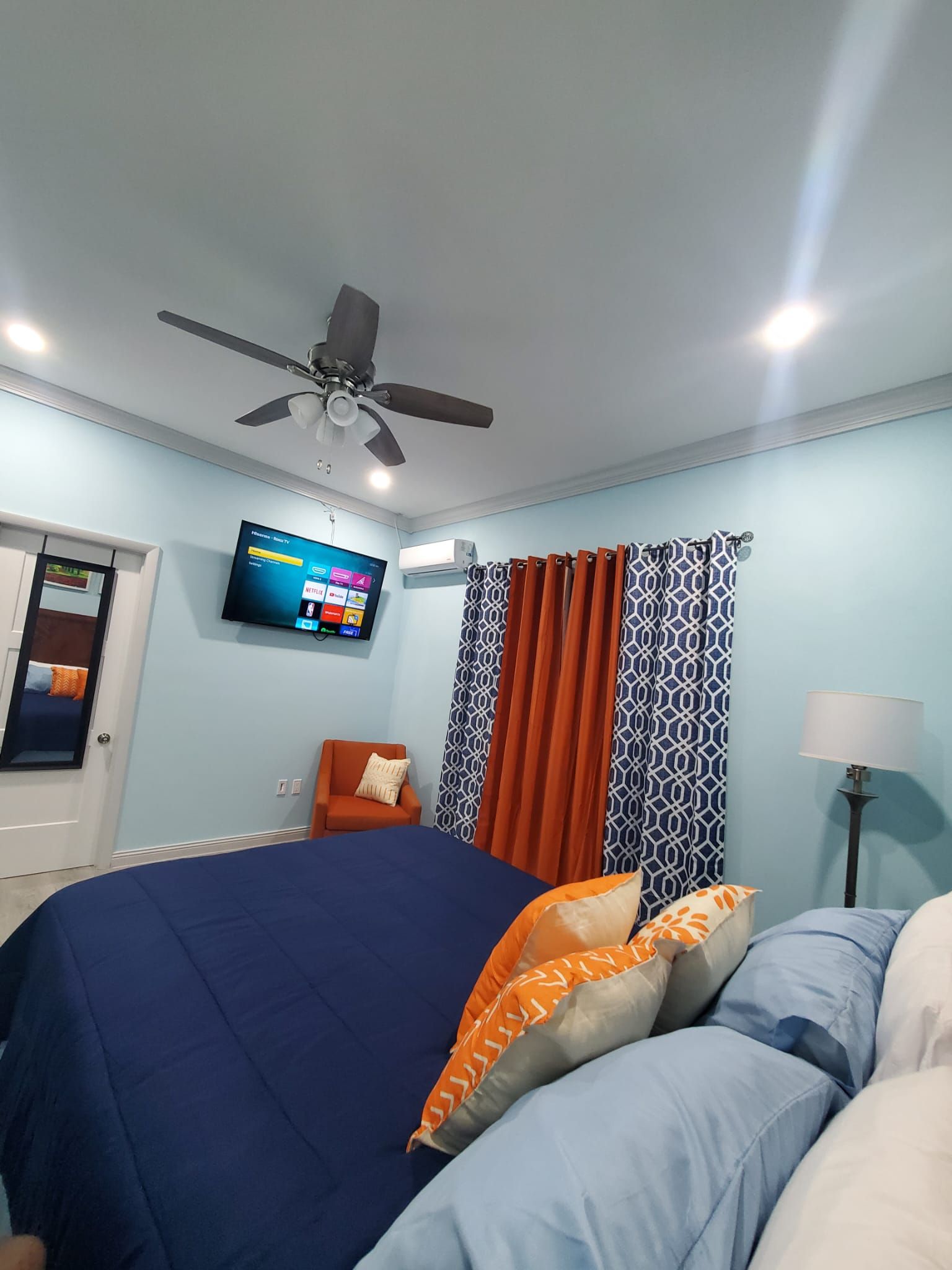 Une chambre à coucher avec un lit, une chaise, un téléviseur et un ventilateur de plafond.