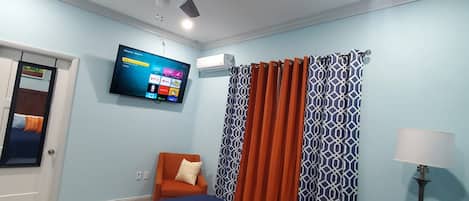 A bedroom with a bed, a chair, a television, and a ceiling fan.