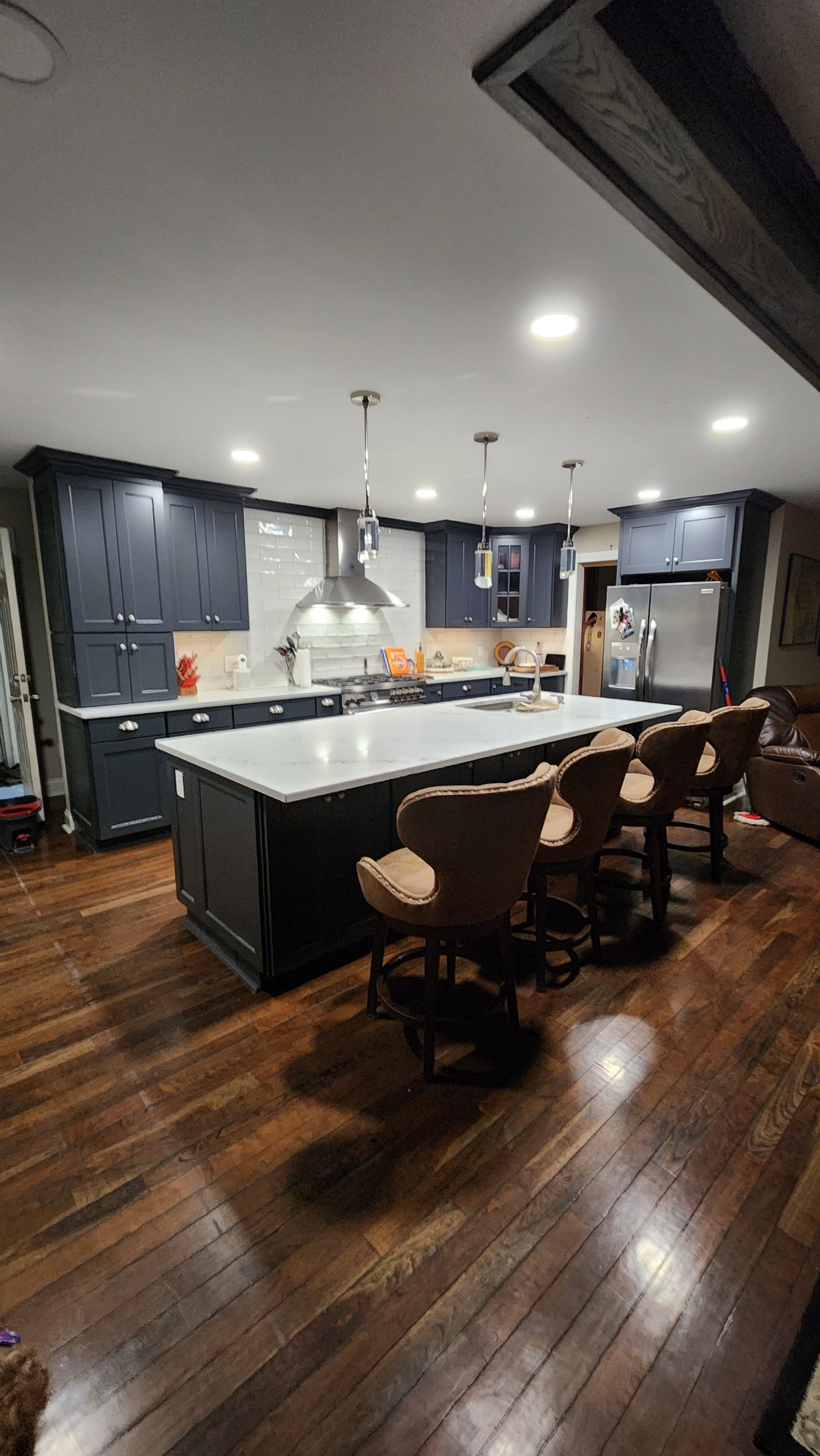 Une cuisine moderne avec des meubles de rangement aux couleurs sombres, un îlot central doté de tabourets de bar et un réfrigérateur en acier inoxydable.