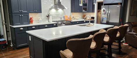 Une cuisine moderne avec des meubles de rangement aux couleurs sombres, un îlot central doté de tabourets de bar et un réfrigérateur en acier inoxydable.