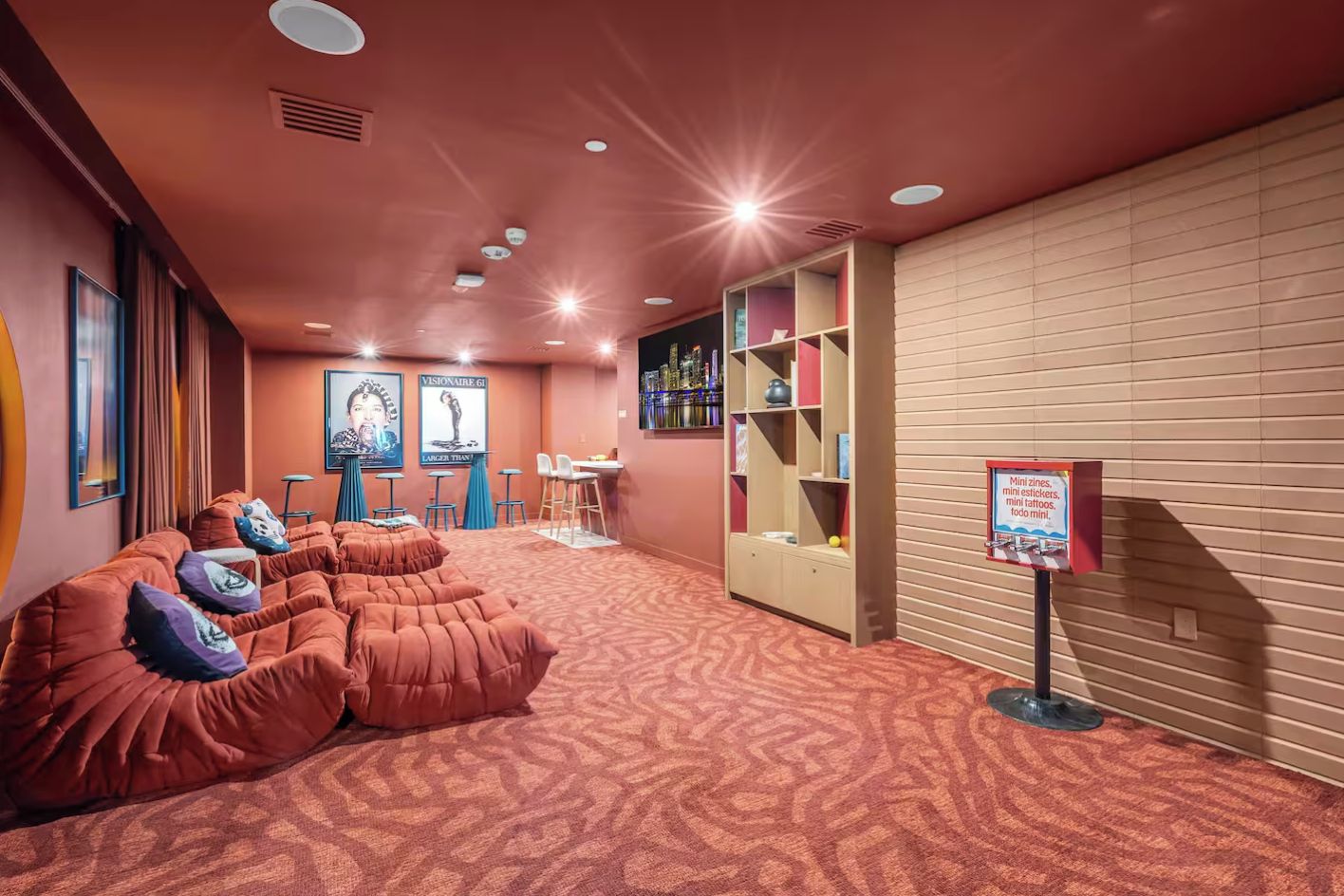 A room with a patterned carpet, a seating area with cushions, a small table with chairs, and a bookshelf.