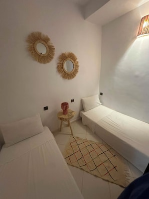 A room with two beds, a small round table, and two wall-mounted mirrors.