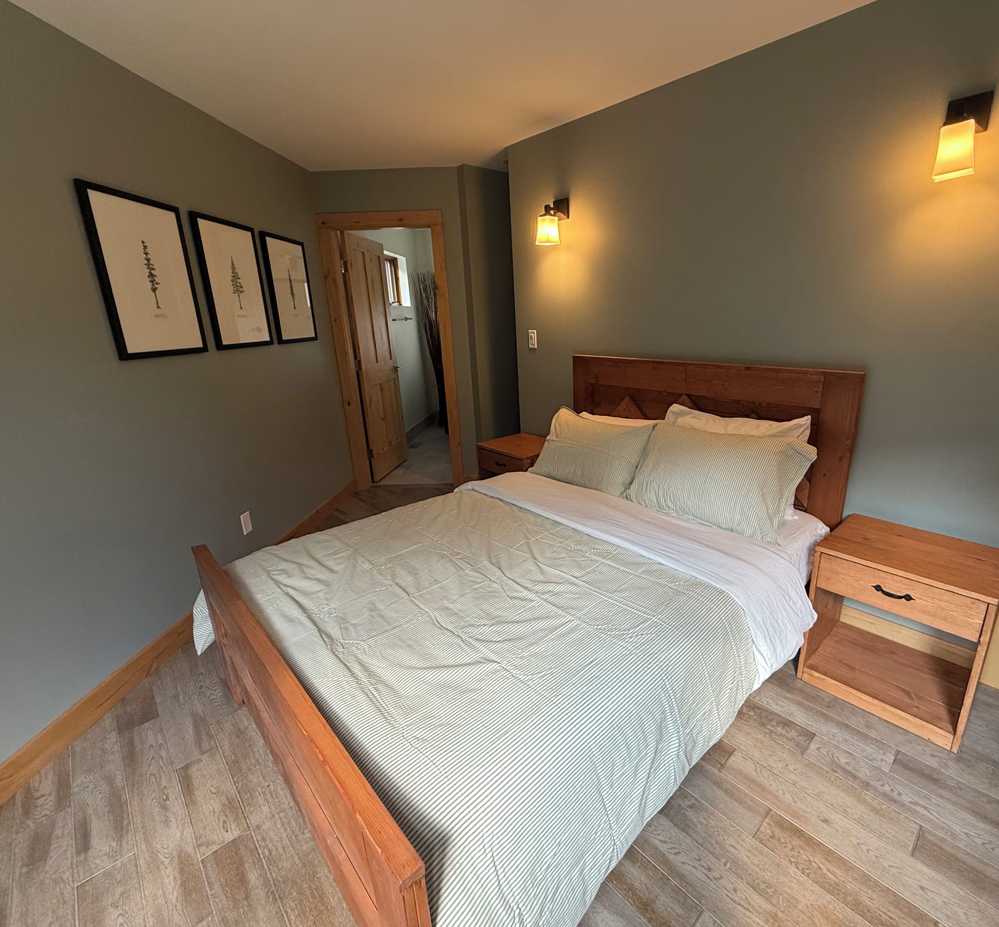 A bedroom with a wooden bed, nightstands, a wooden floor, and a door leading to another room.