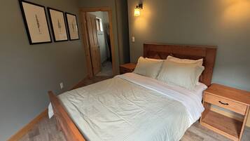A bedroom with a wooden bed, nightstands, a wooden floor, and a door leading to another room.