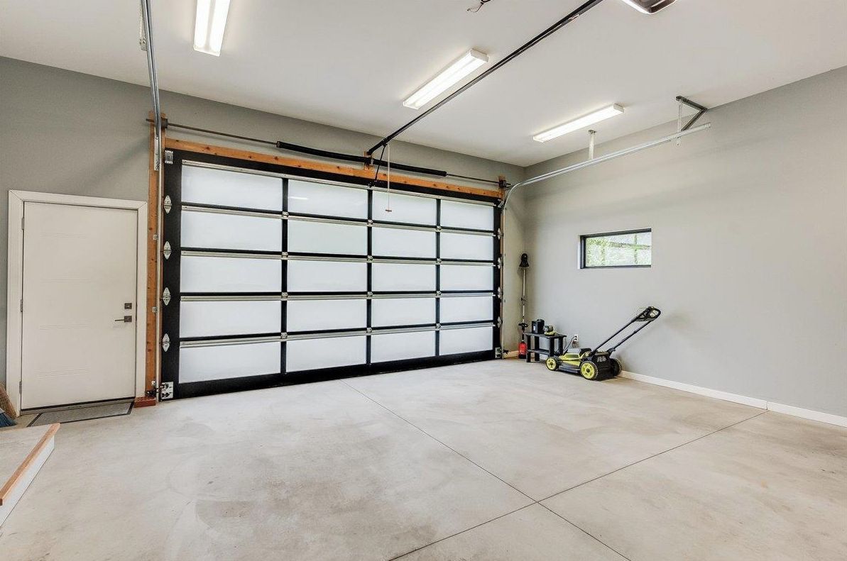 A garage with a large garage door, fluorescent lighting, and a lawnmower.