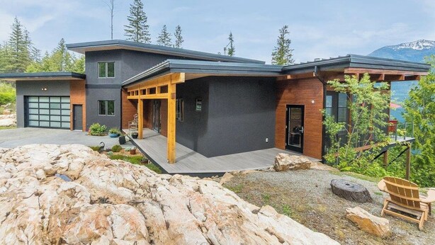 A modern two-story house with a garage, a covered porch, and a view of a mountainous landscape.
