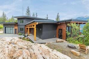 A modern two-story house with a garage, a covered porch, and a view of a mountainous landscape.