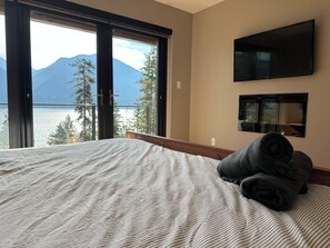 A hotel room with a bed, a TV, and a view of mountains and trees.