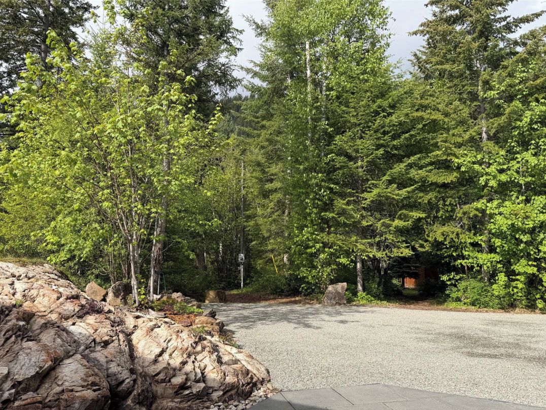 A paved driveway leading into a forested area with a rocky outcrop on the left.