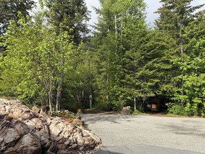 A paved driveway leading into a forested area with a rocky outcrop on the left.