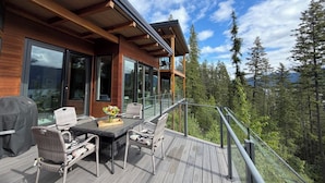 A wooden deck with outdoor furniture and a glass balustrade overlooking a forested area.