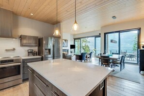 Une cuisine moderne dotée d’un grand îlot central, d’appareils électroménagers en acier inoxydable et de luminaires suspendus.
