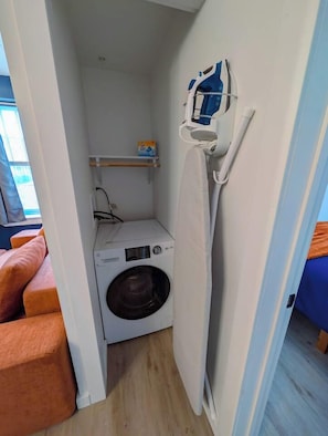 A compact laundry area with a washing machine and a drying rack. - 1 Bdrm Gem: Walkable, Downtown, Queen Bed (Detroit)