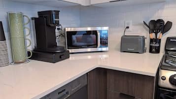 A modern kitchen with a built-in dishwasher, a coffee maker, a microwave, a toaster, and a stove.