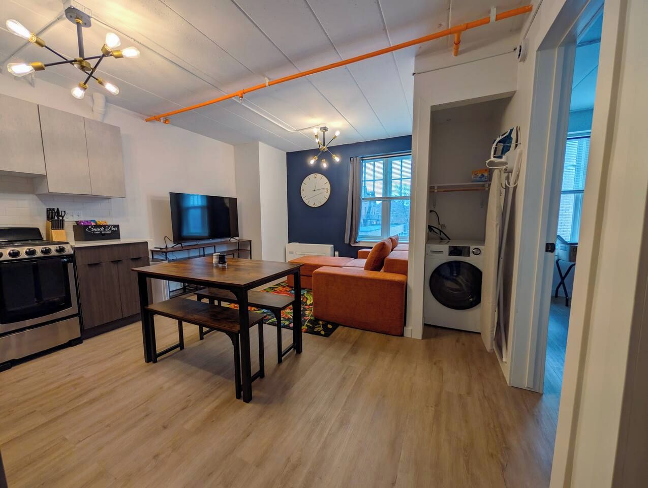 A compact kitchen with a dining area, a washing machine, and a TV.