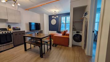 A compact kitchen with a dining area, a washing machine, and a TV.