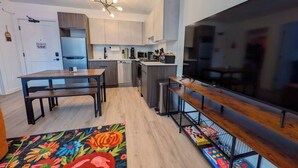 A modern kitchen with a dining area, a large flat-screen TV, and a colorful rug. - 1 Bdrm Gem: Walkable, Downtown, Queen Bed (Detroit)