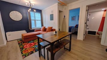 A room with a wooden dining table, a sofa, a clock, and a window.