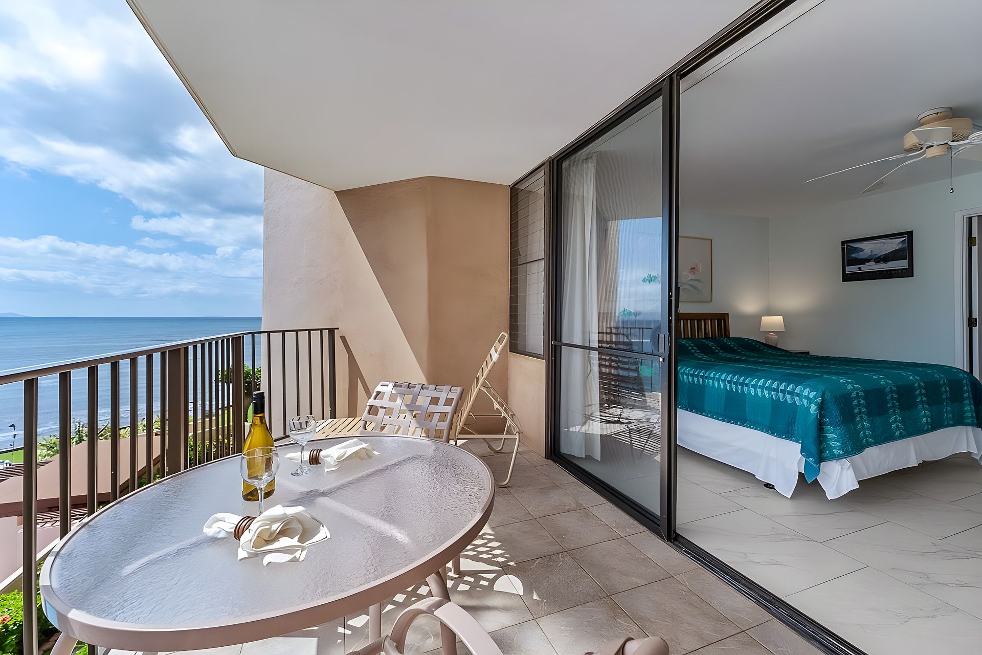 A balcony with a table, chairs, and a bottle of wine.