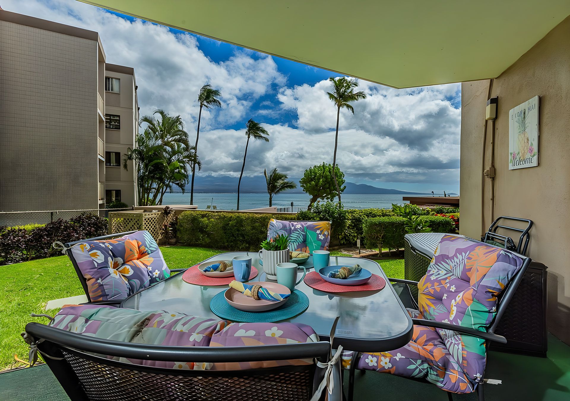 Uma área de refeições ao ar livre com vista para o mar, mobiliada com cadeiras coloridas e uma mesa posta para dois.