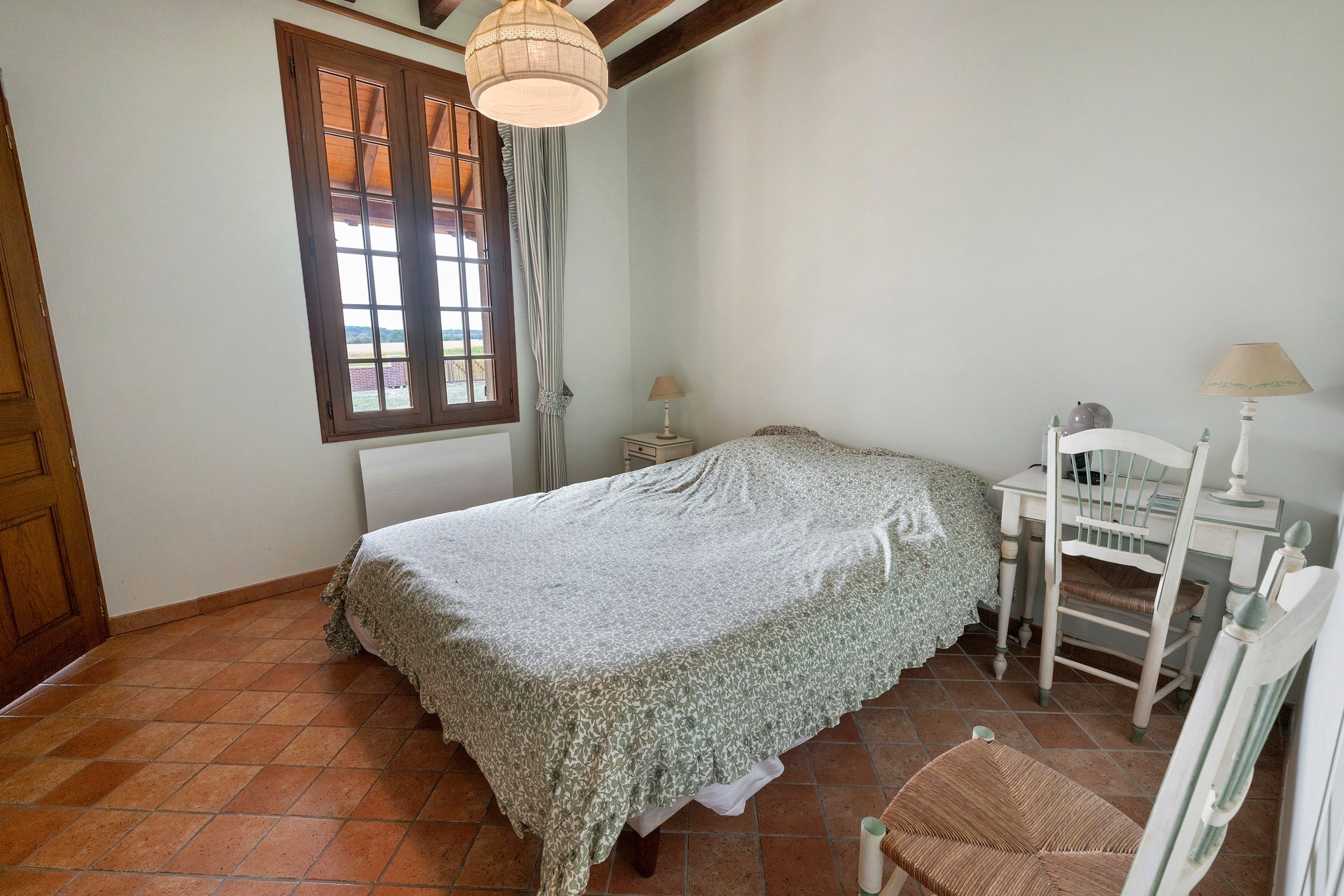 A bedroom with a bed, a chair, a nightstand, a lamp, and a window with curtains.