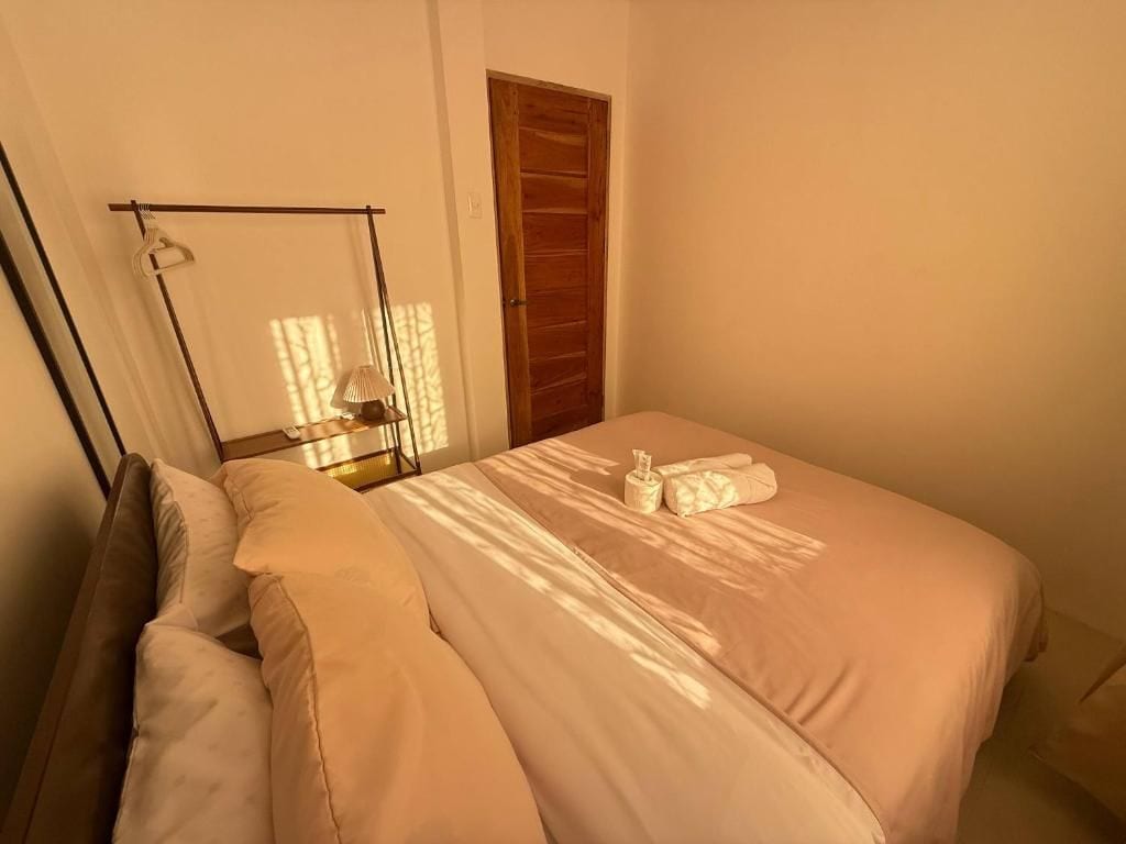 Un dormitorio con una cama, almohadas, una mesita de noche con una lámpara y una puerta de madera.