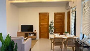 Una sala de estar moderna con un televisor de pantalla plana, un sofá, una mesa de comedor con sillas y una zona de cocina con microondas.