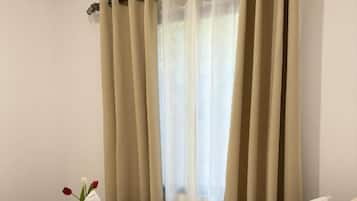 A hotel room with a bed, beige curtains, a white air conditioning unit, and a towel with flowers on the bed.
