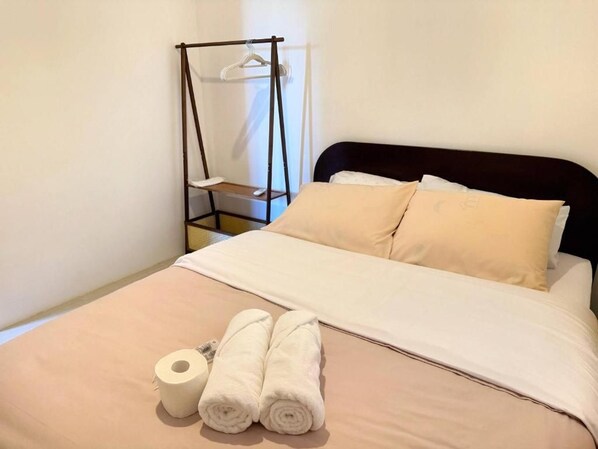 A neatly made bed with two pillows, a hanging chair, and a roll of toilet paper.