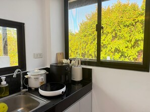 A kitchen with a sink, a coffee maker, a rice cooker, and a window with a view of trees. - Casa Apollo Suites (Puerto Princesa City)