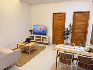 Una sala de estar con televisión, computadora portátil, mesa de comedor con sillas y un sofá.