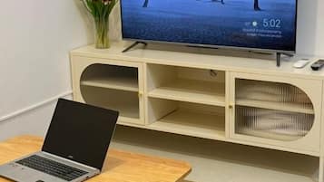 Una habitación con una televisión sobre un mueble, un ordenador portátil sobre una mesa y un florero con flores.
