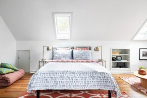 A bedroom with a bed, bedside tables, a desk, a chair, a window, and a shelf with items.