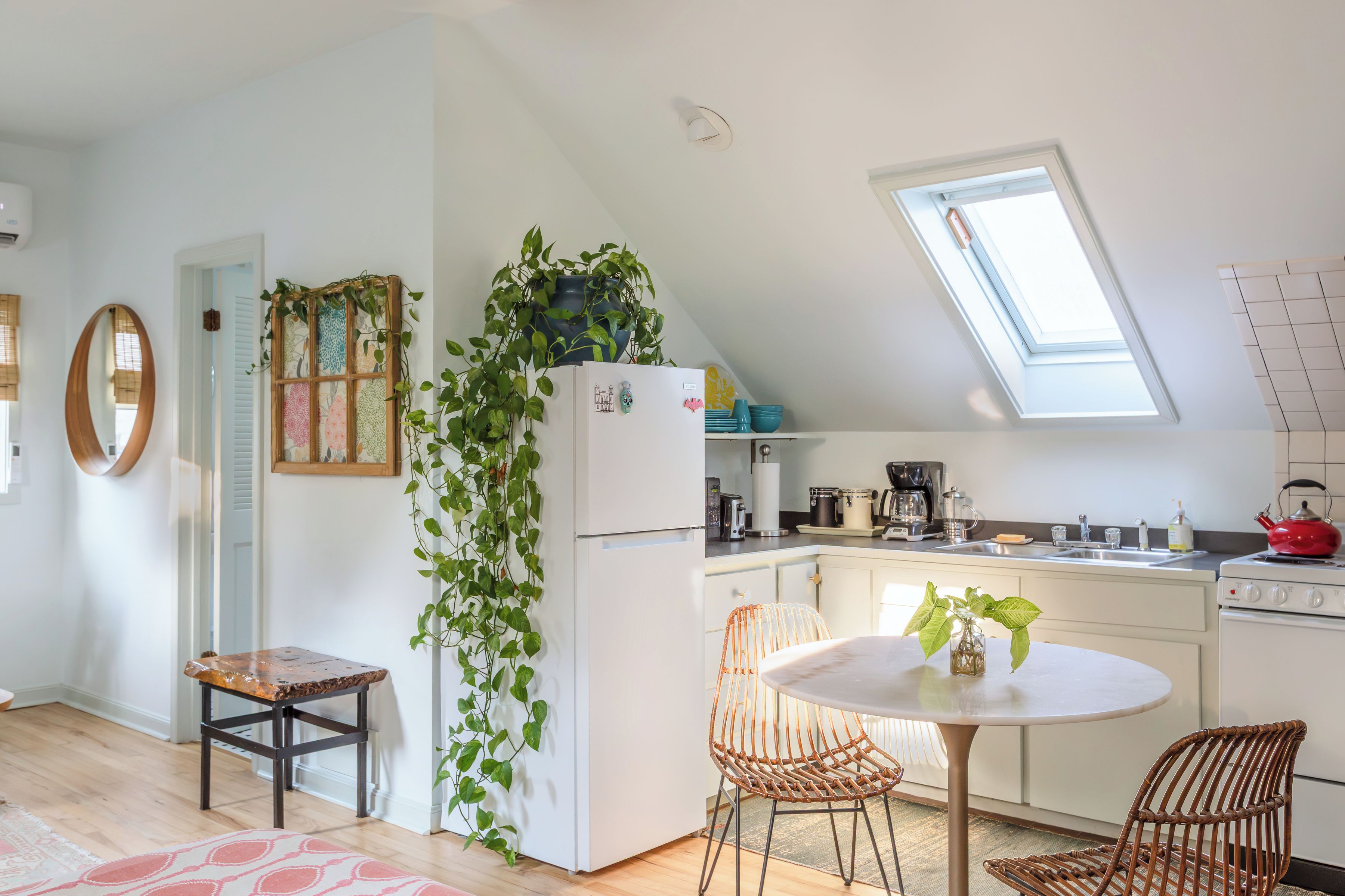 Une cuisine moderne dotée d’une verrière, de meubles blancs et d’un coin repas avec des chaises en osier.