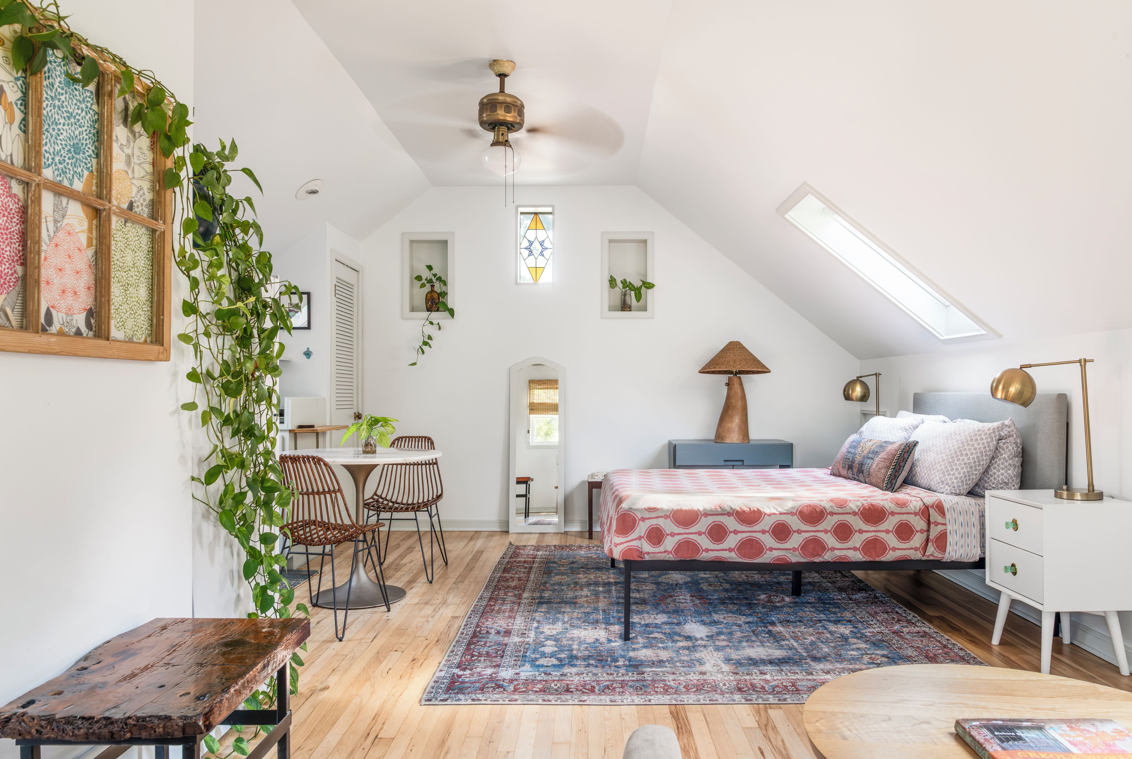 Une chambre à coucher confortable aménagée en mezzanine, avec un plafond en pente, un lit avec une literie à motifs, un bureau avec une chaise et un coin repas avec une table et des chaises.