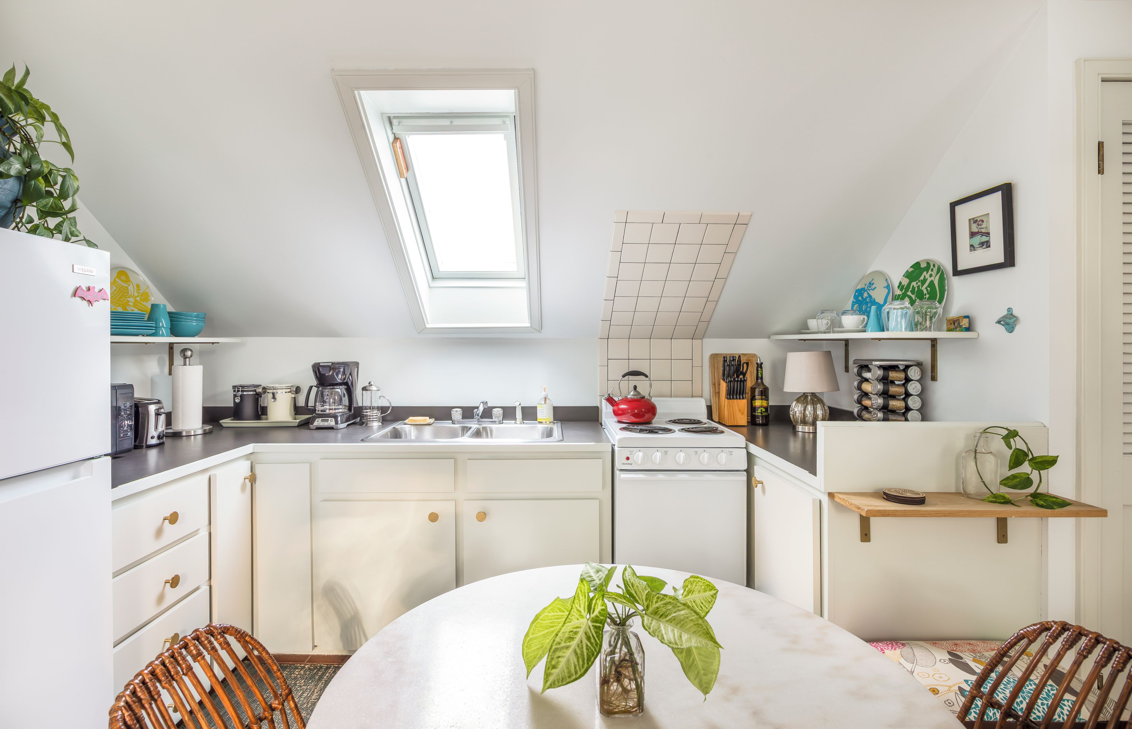 Une cuisine moderne dotée d’une verrière, de meubles blancs et d’un coin repas avec une table et des chaises.