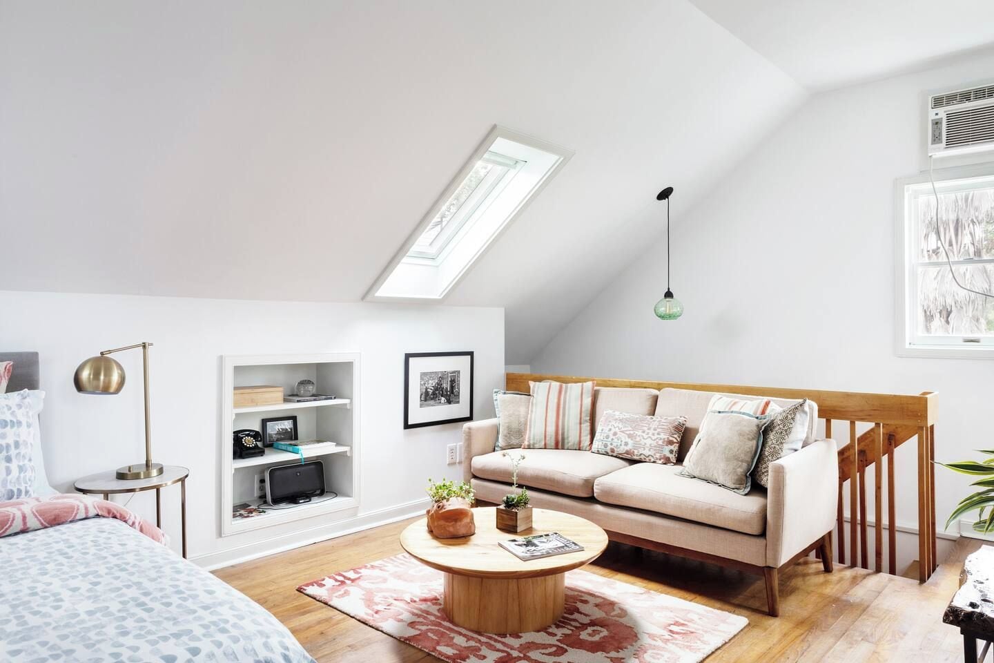 A modern loft bedroom with a sloped ceiling, a built-in desk, a sofa, and a coffee table.