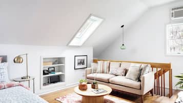 A modern loft bedroom with a sloped ceiling, a built-in desk, a sofa, and a coffee table.
