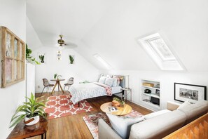 A loft-style bedroom with a sloped ceiling, a bed, a desk, and a seating area.