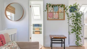 A room with a round mirror, a door leading to a storage area with wicker baskets, a small wooden table, and a wall-mounted plant.