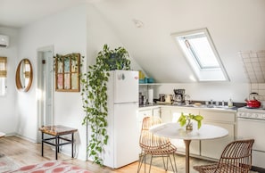 Una cocina moderna con un refrigerador blanco, una mesa de comedor con sillas, una tetera roja y un tragaluz.