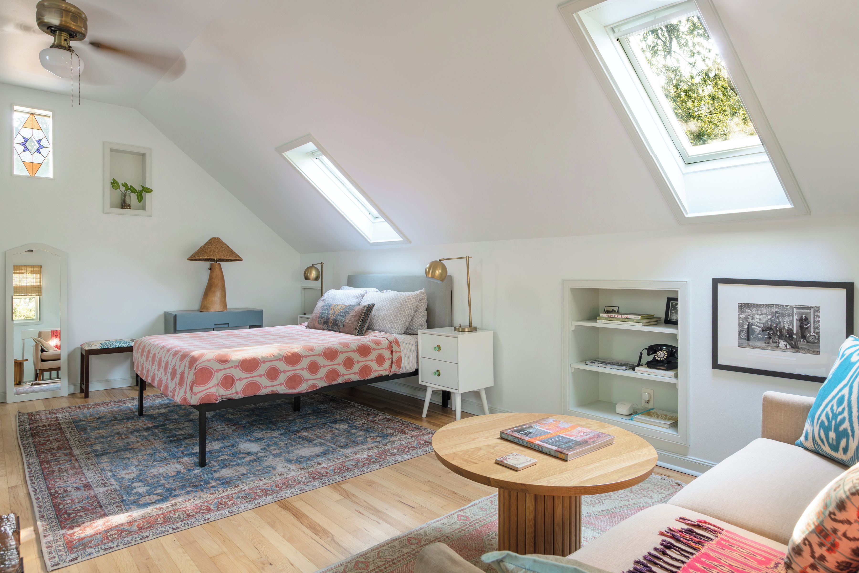 A bedroom with a bed, bedside tables, a desk, a chair, a round coffee table, a bookshelf, and a skylight.