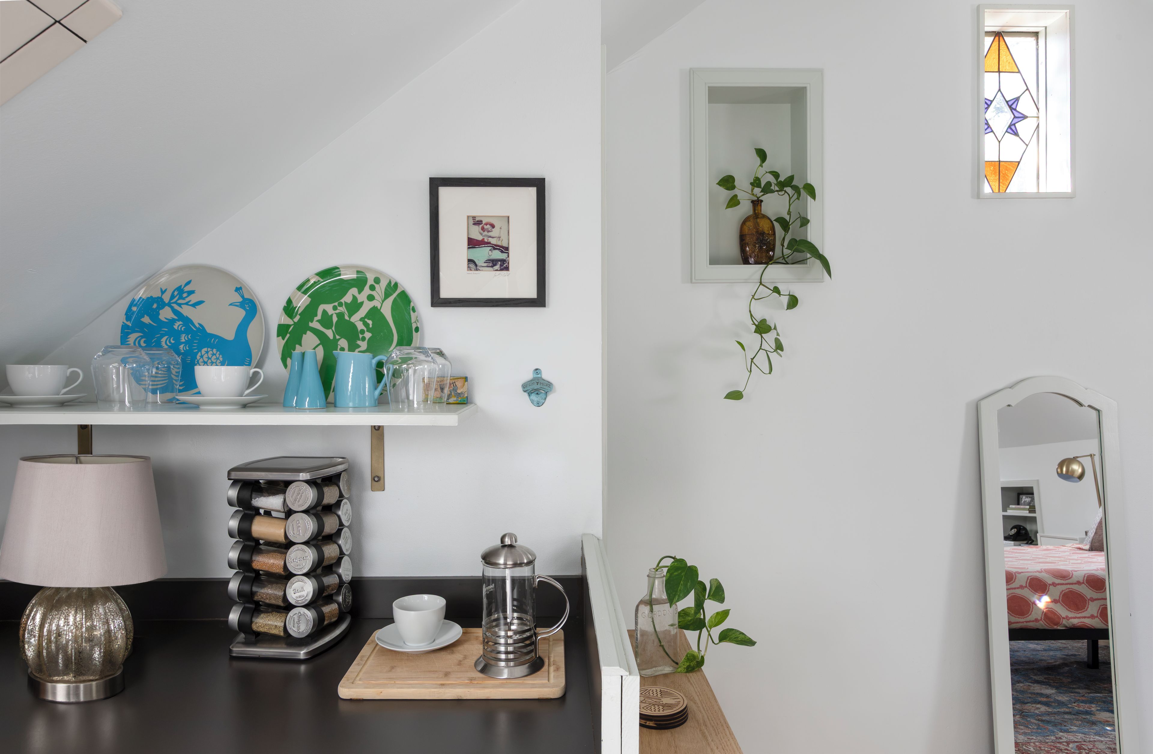 A kitchen area with a coffee maker, a stack of spice jars, a teapot, and a framed picture on the wall.